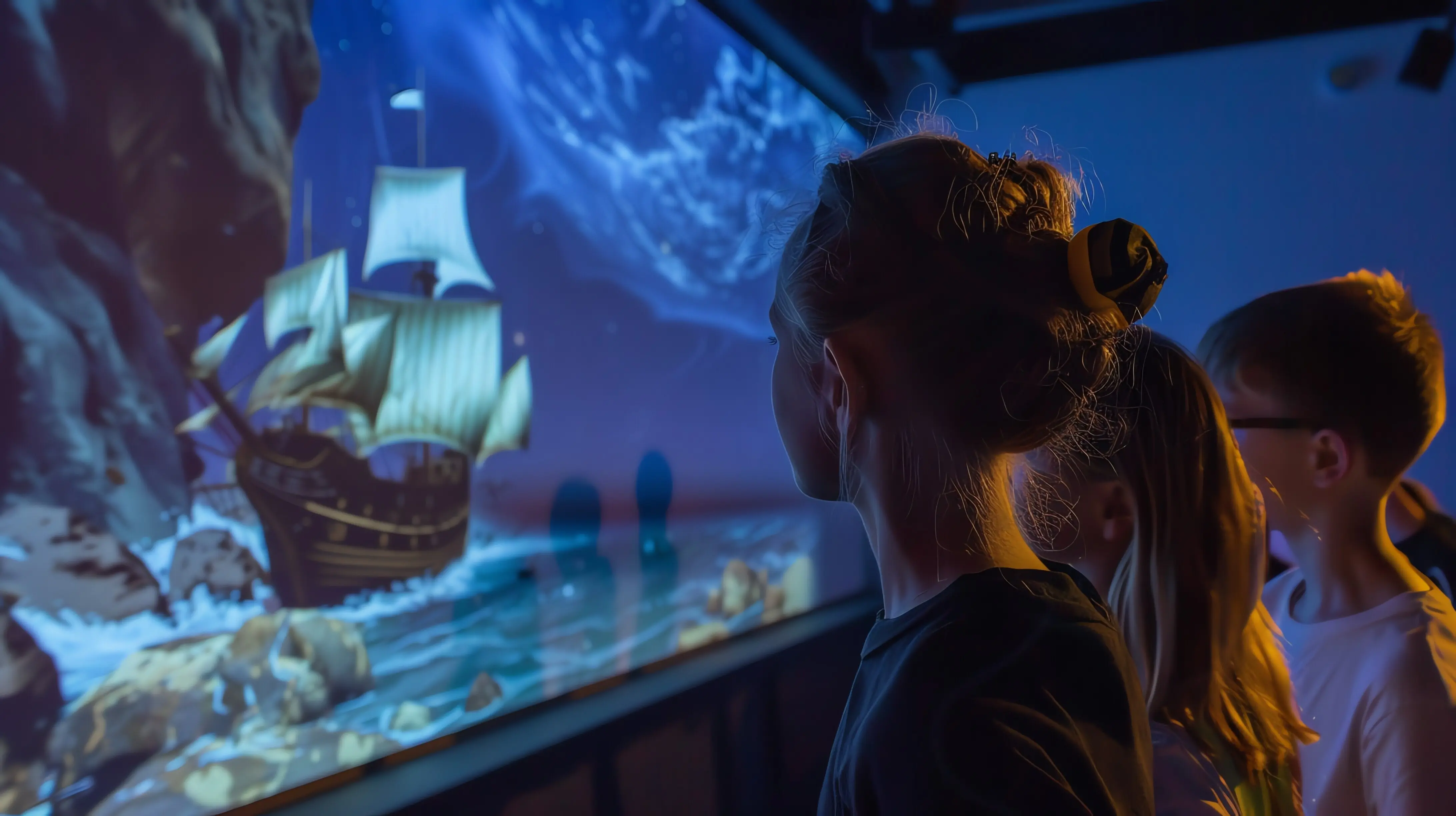 Eine Gruppe von Kindern schaut auf einen großen Bildschirm, auf dem ein Schiff über das Meer segelt.
